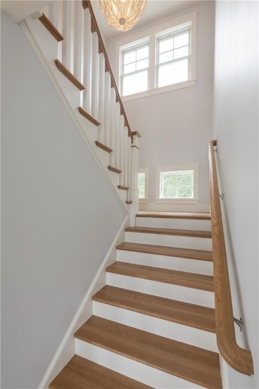 stairs featuring wood-type flooring, a towering ceiling, and an inviting chandelier