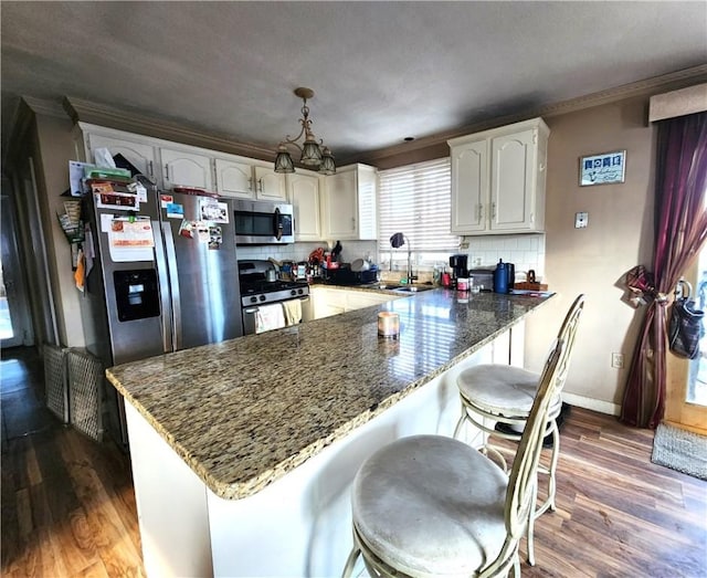 kitchen featuring white cabinetry, stainless steel appliances, tasteful backsplash, dark hardwood / wood-style floors, and kitchen peninsula