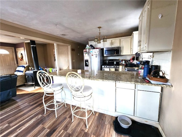 kitchen with backsplash, appliances with stainless steel finishes, decorative light fixtures, dark hardwood / wood-style flooring, and kitchen peninsula