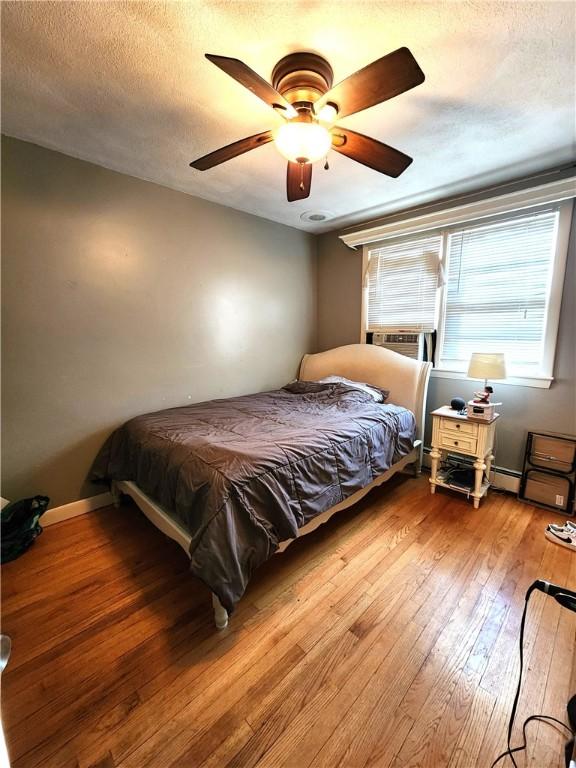 bedroom featuring hardwood / wood-style floors, a textured ceiling, ceiling fan, and cooling unit