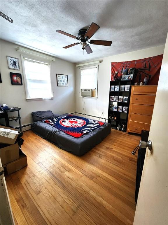 bedroom with ceiling fan, cooling unit, a textured ceiling, and hardwood / wood-style flooring