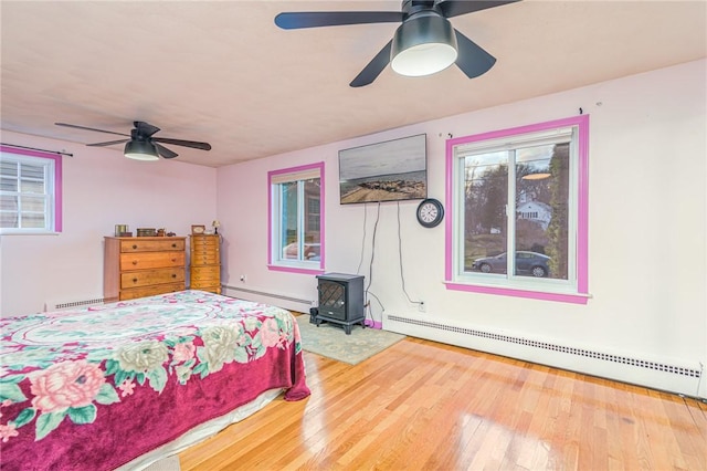 bedroom with hardwood / wood-style flooring, ceiling fan, a wood stove, and baseboard heating