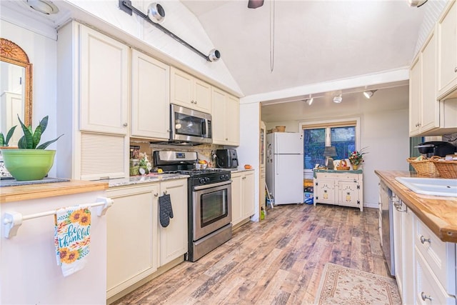 kitchen with backsplash, light wood-type flooring, stainless steel appliances, vaulted ceiling, and butcher block countertops