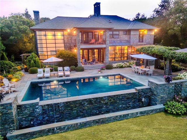 back of house with a chimney, an outdoor pool, a patio, and a balcony