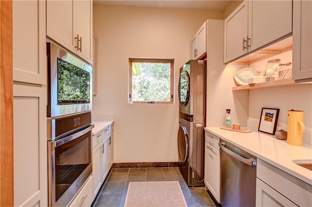 kitchen featuring stainless steel appliances, stacked washer and dryer, light countertops, and baseboards