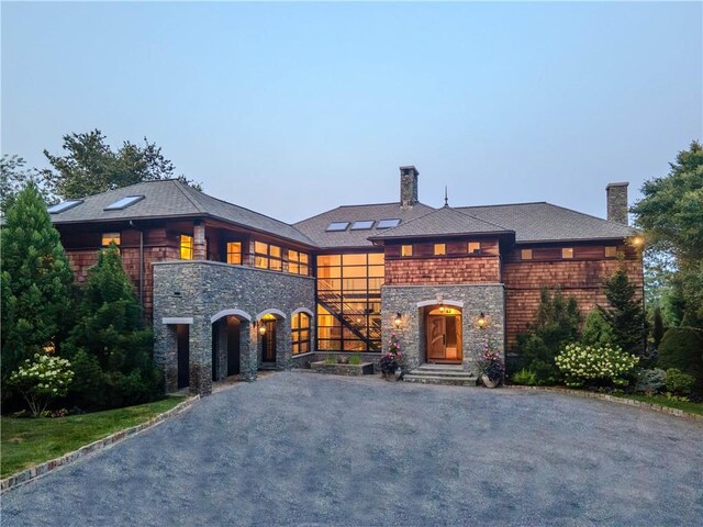 view of front of house featuring aphalt driveway, a chimney, a balcony, and roof mounted solar panels