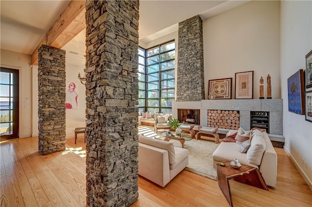 living room with a fireplace with raised hearth, a high ceiling, wood finished floors, baseboards, and ornate columns