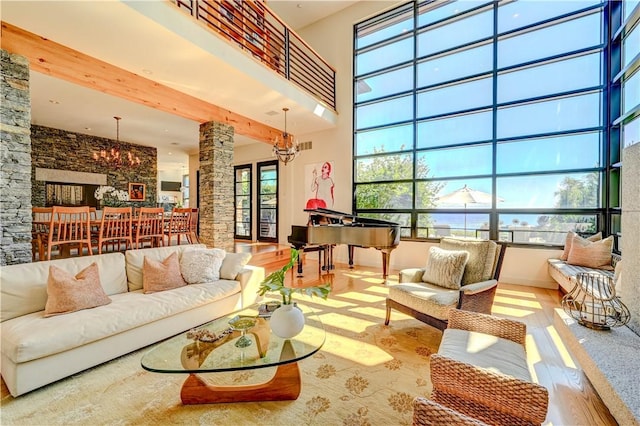 living area with ornate columns, wood finished floors, a towering ceiling, and a notable chandelier