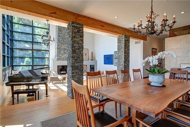 dining space featuring visible vents, wood finished floors, a notable chandelier, a fireplace, and beam ceiling