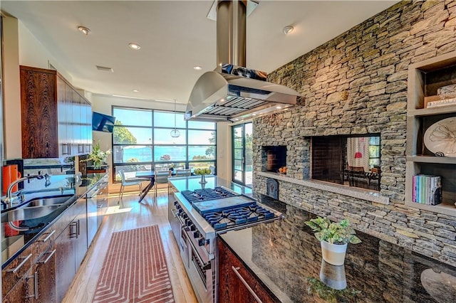 kitchen with a fireplace, island exhaust hood, light wood finished floors, a sink, and double oven range