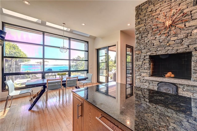 kitchen featuring pendant lighting, brown cabinets, a fireplace, dark stone counters, and light wood-type flooring