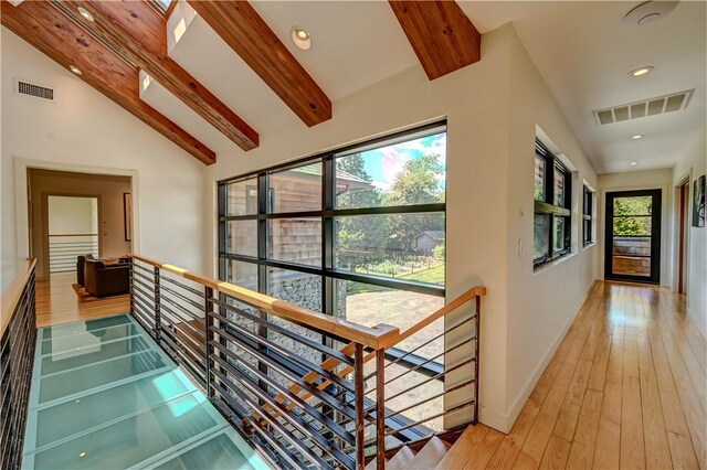 hallway with light wood-style floors, visible vents, lofted ceiling with beams, and an upstairs landing