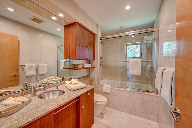 bathroom with toilet, visible vents, vanity, tiled shower / bath, and tile walls