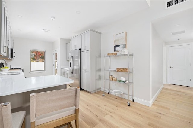 kitchen featuring sink, light hardwood / wood-style flooring, kitchen peninsula, stainless steel fridge, and a breakfast bar