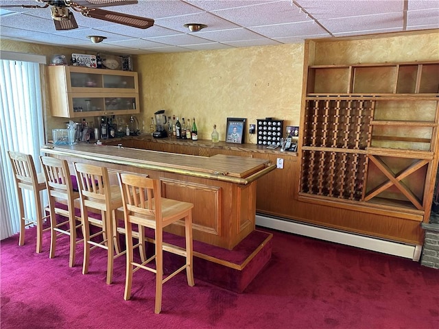 bar featuring baseboard heating, ceiling fan, a drop ceiling, and dark colored carpet