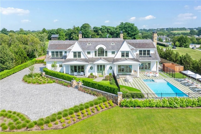 rear view of property featuring a fenced in pool, a patio area, and a lawn