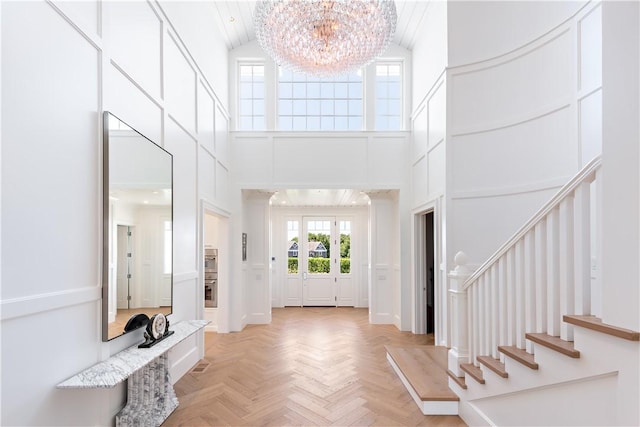 entryway with a chandelier, a towering ceiling, and light parquet floors