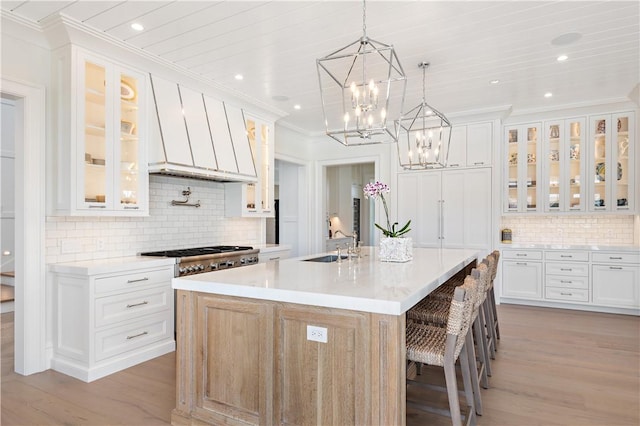 kitchen featuring sink, decorative backsplash, a center island with sink, white cabinets, and light wood-type flooring