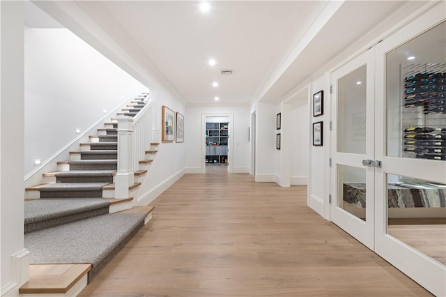 hallway featuring french doors, light wood-type flooring, and crown molding