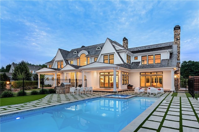 rear view of property featuring a swimming pool with hot tub, an outdoor living space, an outdoor kitchen, and a patio area