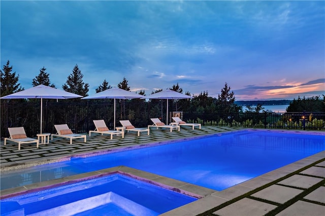 pool at dusk with an in ground hot tub and a water view