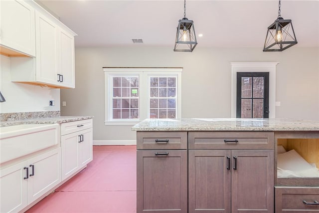 kitchen featuring white cabinets, sink, decorative light fixtures, a kitchen island, and light stone counters