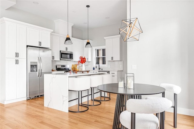 kitchen with a center island, hanging light fixtures, stainless steel appliances, light hardwood / wood-style floors, and white cabinets