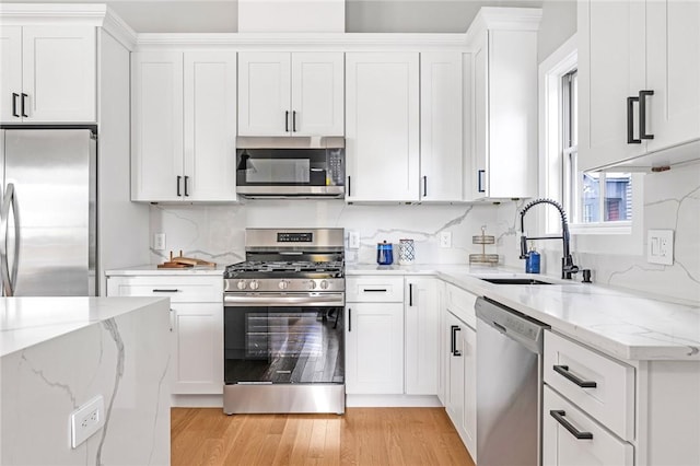 kitchen with white cabinets, stainless steel appliances, light stone countertops, and sink