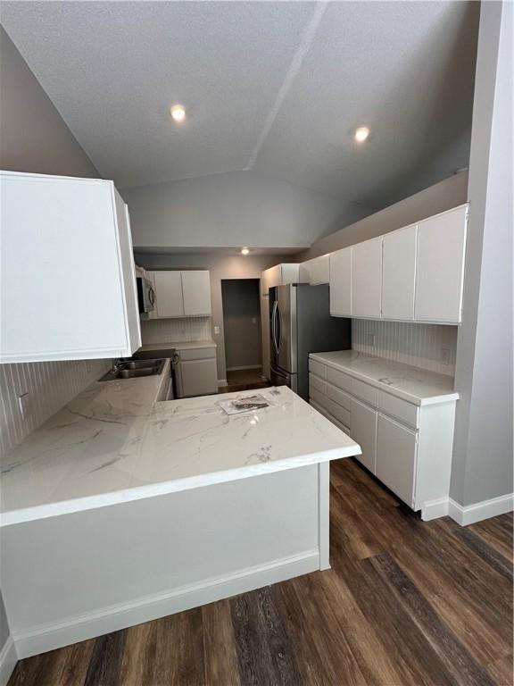 kitchen featuring white cabinets, vaulted ceiling, tasteful backsplash, kitchen peninsula, and stainless steel refrigerator