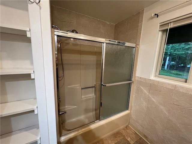 bathroom featuring shower / bath combination with glass door and tile walls