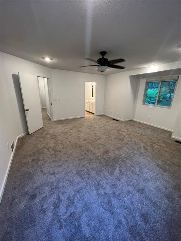 spare room featuring ceiling fan and dark carpet