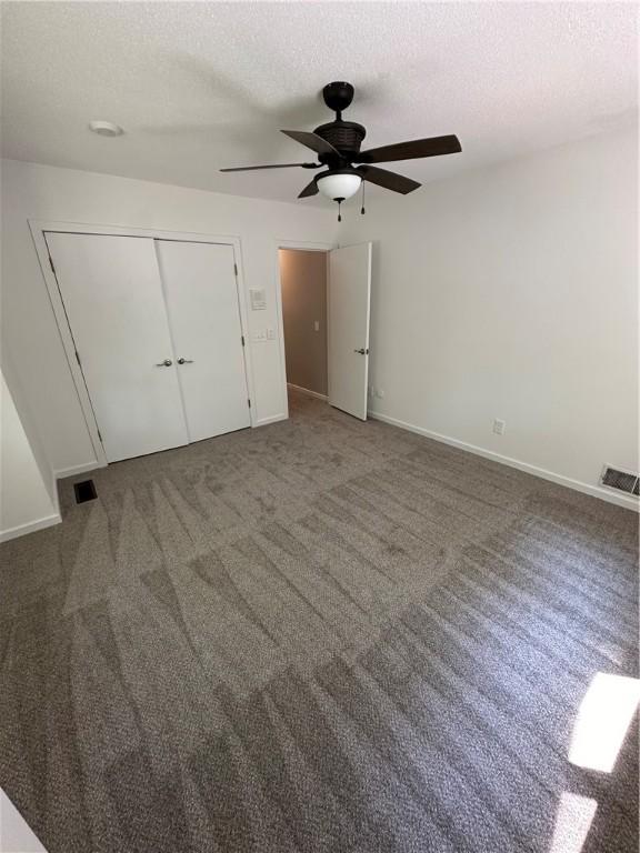 unfurnished bedroom featuring ceiling fan, dark carpet, a textured ceiling, and a closet