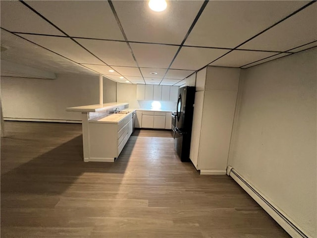 kitchen with black refrigerator, dark wood-type flooring, sink, a baseboard radiator, and white cabinets