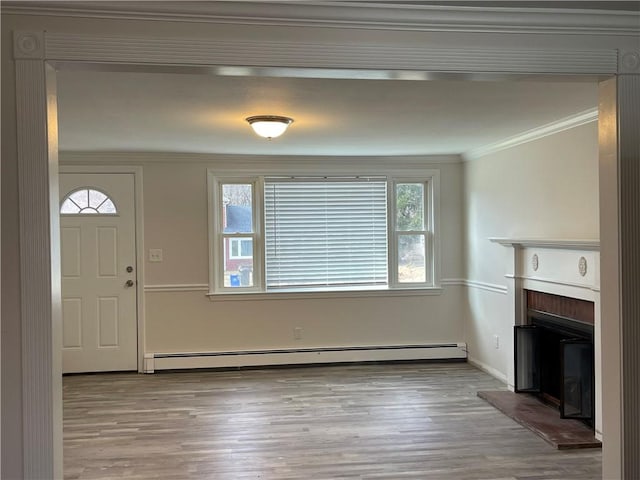 foyer entrance featuring a baseboard heating unit, light hardwood / wood-style floors, crown molding, and a brick fireplace