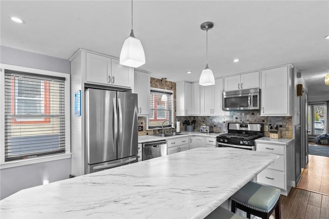 kitchen with white cabinetry, sink, hanging light fixtures, stainless steel appliances, and tasteful backsplash