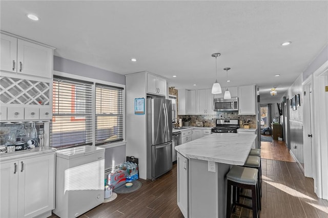 kitchen featuring hanging light fixtures, white cabinetry, backsplash, and appliances with stainless steel finishes