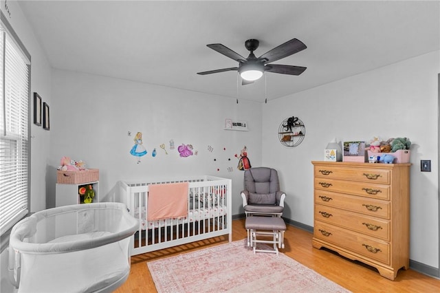 bedroom with ceiling fan, a nursery area, and hardwood / wood-style flooring