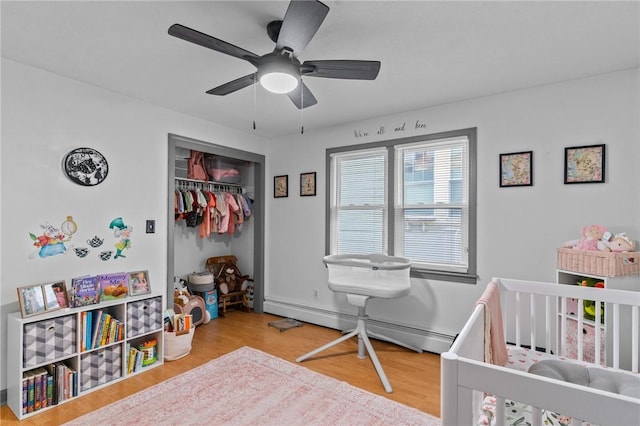 bedroom featuring ceiling fan, hardwood / wood-style flooring, a crib, and a baseboard heating unit