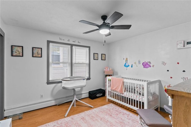 bedroom featuring ceiling fan, a baseboard radiator, a crib, and wood-type flooring