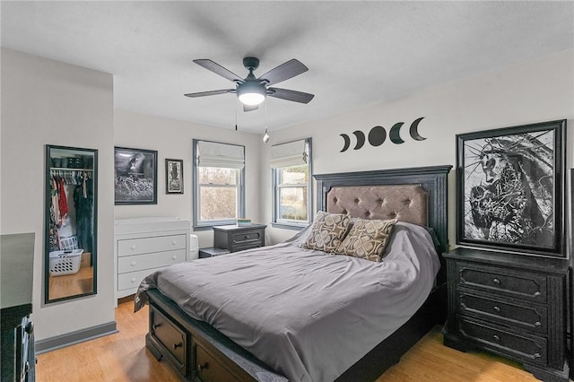 bedroom with a spacious closet, a closet, light hardwood / wood-style flooring, and ceiling fan