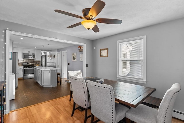 dining space featuring baseboard heating, ceiling fan, and dark wood-type flooring