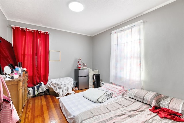 bedroom with multiple windows, stainless steel fridge, hardwood / wood-style floors, and a baseboard heating unit