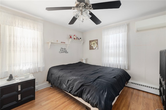 bedroom featuring multiple windows, hardwood / wood-style flooring, ceiling fan, and a baseboard heating unit