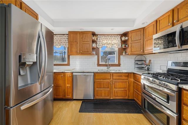 kitchen featuring sink, light hardwood / wood-style flooring, appliances with stainless steel finishes, tasteful backsplash, and light stone counters