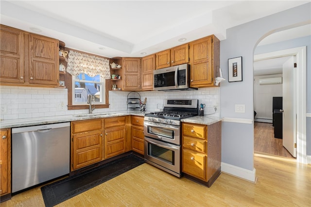 kitchen with light stone counters, sink, appliances with stainless steel finishes, and light hardwood / wood-style flooring