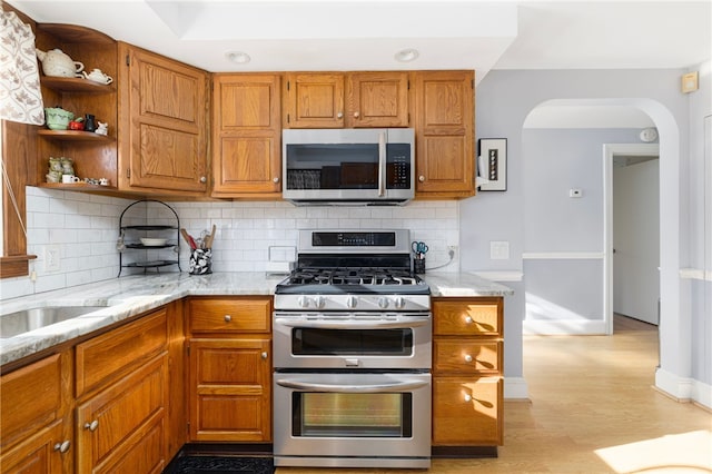 kitchen featuring appliances with stainless steel finishes, backsplash, light hardwood / wood-style flooring, and light stone counters