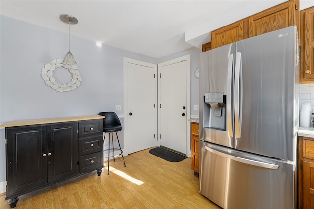 kitchen featuring stainless steel fridge, decorative light fixtures, tasteful backsplash, and light hardwood / wood-style floors