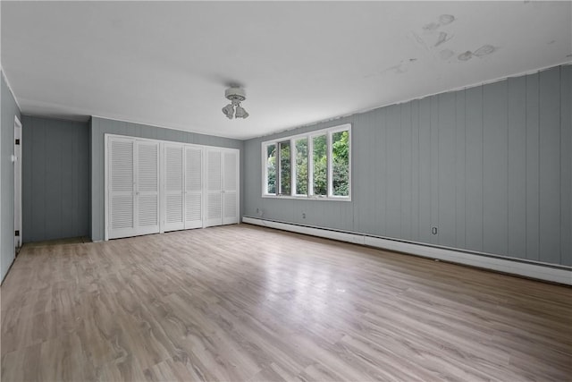 unfurnished bedroom with wood walls, light hardwood / wood-style floors, and a baseboard heating unit