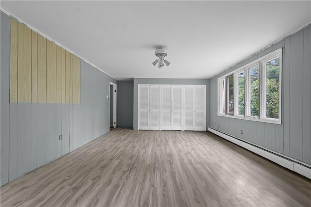 unfurnished living room with baseboard heating, wooden walls, and hardwood / wood-style flooring