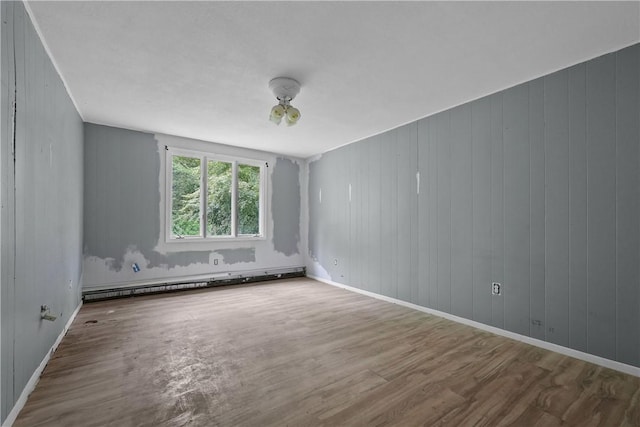 empty room with hardwood / wood-style flooring, wood walls, and baseboard heating